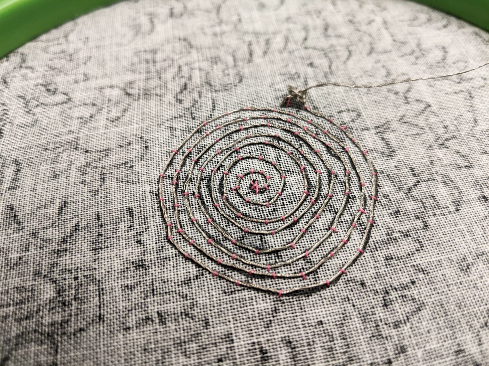 Front view of the soft speaker-stainless steel wire coiled, stitched with pink string, on black cloth held in embroidery frame